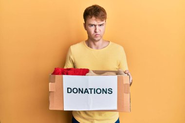 Hayır kurumu için bağış kutusu tutan genç, beyaz bir adam şüpheci ve gergin, sorun yüzünden üzgün. negatif kişi. 