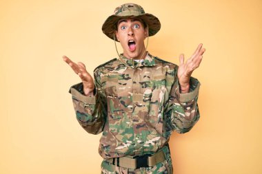 Kamuflaj üniforması giyen genç yakışıklı adam çılgın kutlamalar yapıyor ve başarıya hayret ediyor. Kolları açık, gözleri açık, heyecanla bağırıyor. Kazanan konsept 