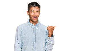 Genç, yakışıklı, Afro-Amerikalı, günlük kıyafetler giymiş, gülümseyen, gülümseyen ve baş parmağıyla yüzünü gösteren bir adam.. 