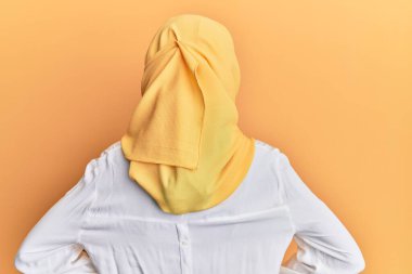 Genç esmer Arap kadın geleneksel İslami başörtüsü takıyor. Arkaya bakıyor ve kollarını vücuduna dikiyor. 