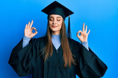 Mezuniyet şapkası ve tören cübbesi takan güzel esmer bir kadın. Gözleri kapalı rahatlayıp parmaklarıyla meditasyon hareketi yapıyor. yoga konsepti. 