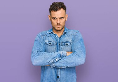 Sıradan kot ceket giyen genç İspanyol adam şüpheci ve gergin, yüzünde çapraz kollu tasvip etmeyen ifade. negatif kişi. 