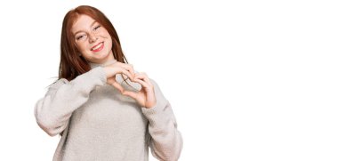 Okuyan, sıradan bir kazak giyen genç bir kadın. Sevgiyle gülümseyen. Elleriyle kalp sembolü ve şekli gösteren. romantik kavram. 