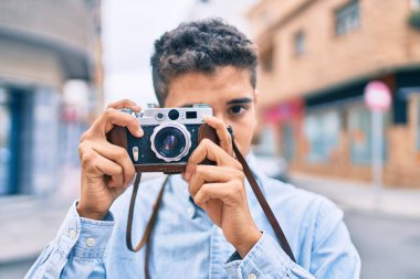 Genç Latin turist mutlu bir şekilde gülümsüyor. Şehirde eski model kamera kullanıyor..