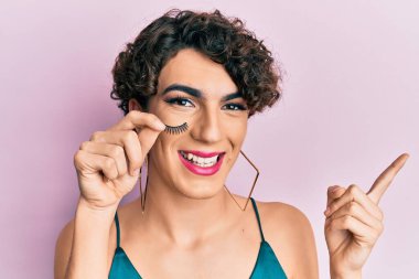 Takma kirpik tutan genç adam gülümseyen mutlu bir şekilde elini ve parmağını yana doğru uzattı. 