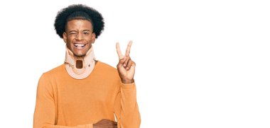 Afro saçlı, boyun tasması takan, kameraya gülümseyen ve zafer işareti yapan Afro-Amerikan bir adam. İki numara.. 