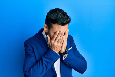 Genç İspanyol iş adamı, ağlarken yüzünü ellerle kapatan üzgün bir ifadeyle iş ceketi giyiyor. depresyon kavramı. 