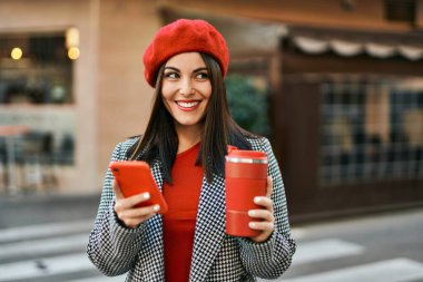 Genç İspanyol kadın akıllı telefon kullanıyor ve şehirde kahve içiyor..