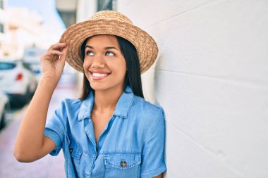 Tatildeki genç Latin turist kız gülümsüyor. Şehrin duvarına yaslanmaktan mutlu..