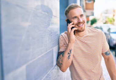 Genç İrlandalı gülümseyen mutlu bir adam şehrin caddesinde akıllı telefonda konuşuyor..