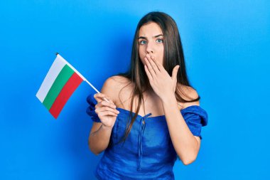 Genç esmer ergen, elinde bulgaria bayrağı tutarak ağzını eliyle kapatıyor, şok geçiriyor ve hata yapmaktan korkuyor. şaşırmış ifade 