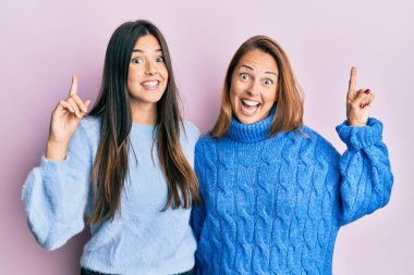 Yün süveter giyen İspanyol anne-kız ailesi şaşkın şaşkın gülüyor ve parmaklarıyla işaret ediyor ve kollarını kaldırıyordu.. 