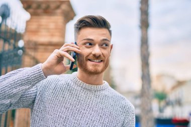 Genç beyaz adam gülümsüyor. Şehirdeki akıllı telefondan konuşuyor..