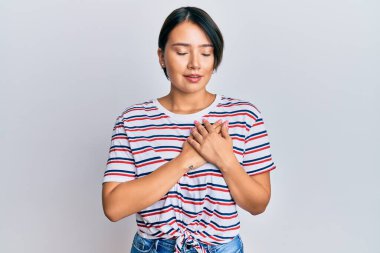 Kısa saçlı, sıradan kıyafetler giyen, elleri göğsünde, gözleri kapalı ve yüzünde minnet dolu bir jest olan güzel bir kadın. sağlık kavramı. 