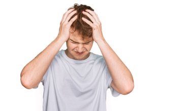 Beyaz günlük tişört giyen genç beyaz bir adam acı ve migren yüzünden çaresiz ve stresli bir baş ağrısı çekiyor. Eller başının üstünde.. 