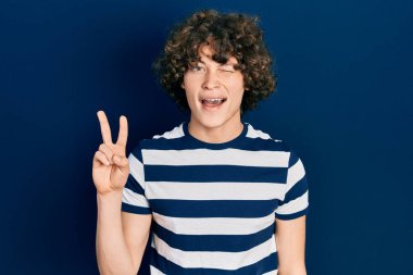 Sıradan çizgili tişört giyen yakışıklı genç adam kameraya bakıp gülümseyen ve zafer işareti yapan. İki numara.. 