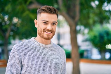 Genç beyaz adam parkta mutlu bir şekilde gülümsüyor..