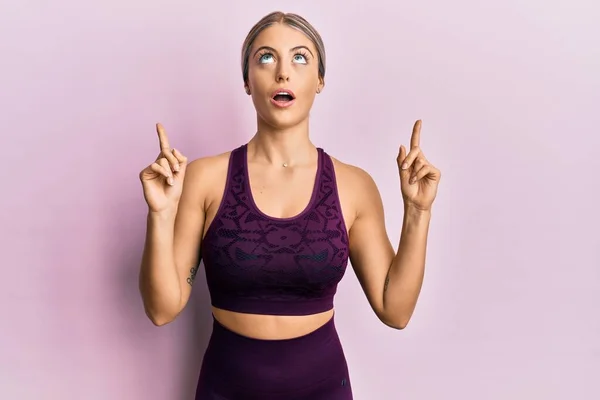 Mulher Loira Bonita Vestindo Sportswear Sobre Fundo Rosa Espantado Surpreso — Fotografia de Stock