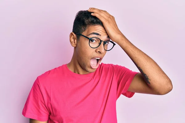 若いハンサムなアフリカ系アメリカ人の男性が誤って頭の上に手で驚いてピンクの背景に眼鏡をかけて エラーを覚えている 忘れられた悪い記憶の概念 — ストック写真