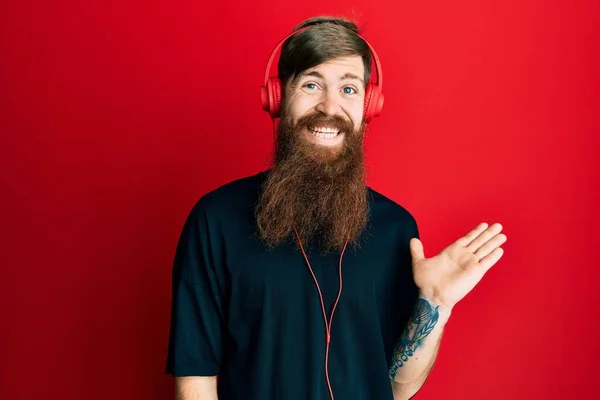 Rudowłosy Mężczyzna Długą Brodą Słuchający Muzyki Przy Użyciu Słuchawek Uśmiechnięty — Zdjęcie stockowe