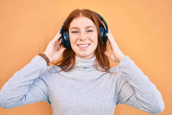 Young irish teenager girl smiling happy listening music using headphones at the city.