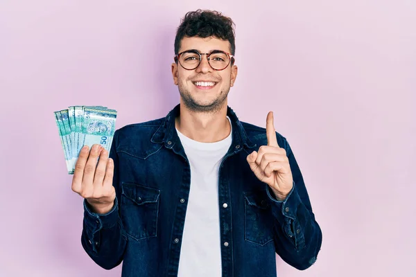 Joven Hispano Sosteniendo Billetes Malaysia Ringgit Sonriendo Con Una Idea —  Fotos de Stock