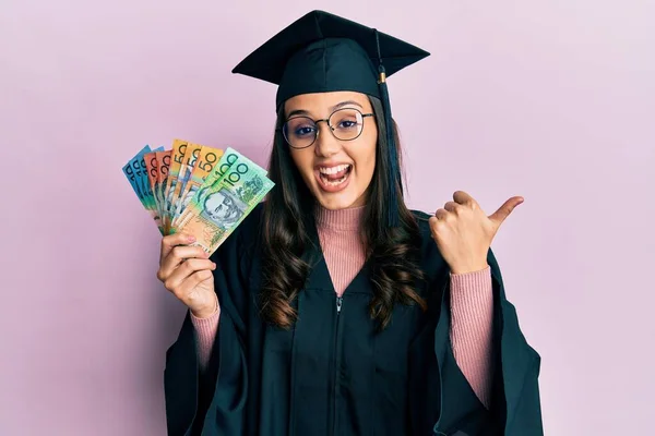 Young Hispanic Woman Wearing Graduation Uniform Holding Australian Dollars Pointing — Stock Photo, Image