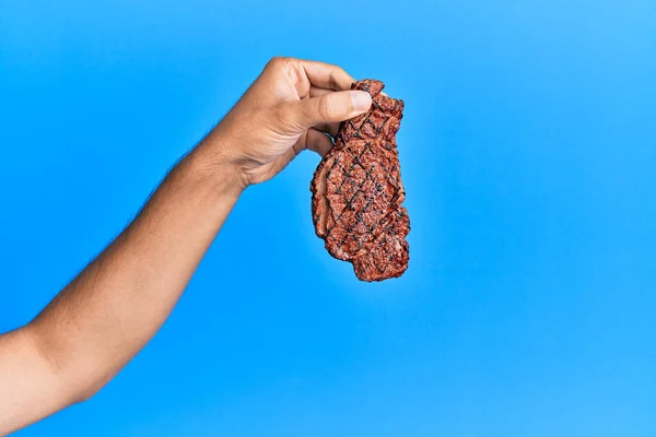 Mano Joven Hispano Sosteniendo Carne Parrilla Sobre Fondo Azul Aislado — Foto de Stock