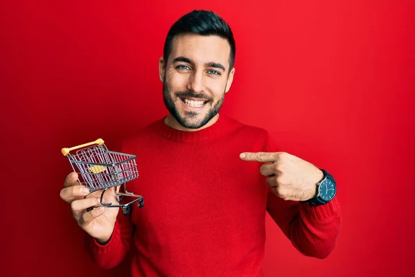 Jovem Hispânico Homem Segurando Pequeno Supermercado Carrinho Compras Apontando Dedo — Fotografia de Stock