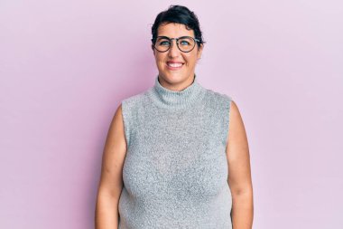 Artı, sıradan kıyafetler ve gözlük takan esmer kadın pozitif ve mutlu görünüyor ve kendine güvenen bir gülümsemeyle dişlerini gösteriyor. 