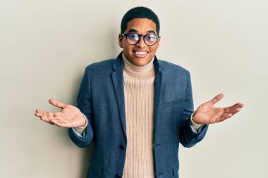 Zarif kıyafetler giyen, gözlüklü, kafası karışık ve kolları ve elleri havada genç, yakışıklı İspanyol bir adam. şüphe kavramı. 