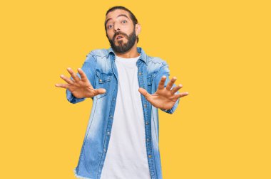 Uzun saçlı ve sakallı çekici bir adam. Sıradan bir kot ceket giyiyor. El hareketlerini durduruyor. 