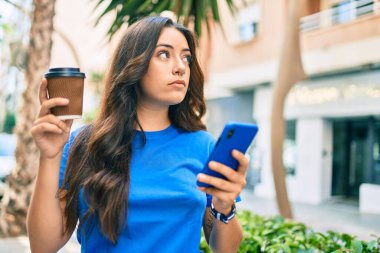 Zeki telefon kullanan ve şehirde kahve içen ciddi yüzlü İspanyol bir kadın..