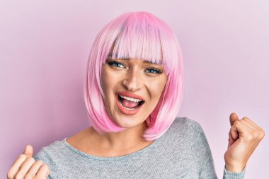 Pembe peruklu genç beyaz kadın gururla bağırıyor zaferi ve başarıyı kutluyor. Kollarını kaldırarak heyecanlanıyor. 