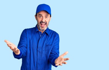 Orta yaşlı yakışıklı tamirci üniforması giyen neşeli kollarını açıp gülümseyen hoş geldin, pozitif ve kendinden emin selamlar. 