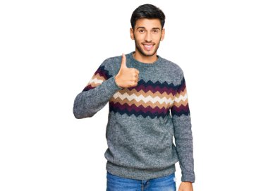 Kış süveteri giyen genç yakışıklı adam elleriyle mutlu bir jest yapıyor. Kameraya bakıp başarıyı gösteren ifade. 