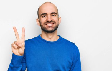 Gündelik kıyafetler giyen genç İspanyol adam iki numarayı gösterip işaret ederken kendinden emin ve mutlu bir şekilde gülümsüyor.. 