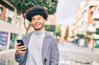 Genç Afrikalı Amerikalı iş adamı şehirde akıllı telefon kullanarak mutlu bir şekilde gülümsüyor..