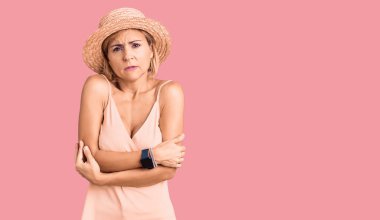 Yaz şapkası takan genç sarışın kadın kış soğuğu için titriyor ve donuyor. Yüzünde üzgün ve şok ifadesi var. 