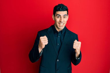 İş kıyafetleri giymiş yakışıklı İspanyol adam kollarını kaldırıp, gözlerini açarak başarıyı kutluyor ve şaşırıyor. Kazanan konsept. 