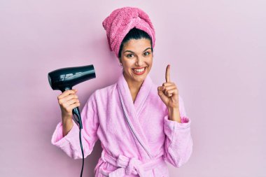 Duşta bornoz giyen genç İspanyol kadın kurutucu kullanıyor. Bir fikir veya soruyla gülümsüyor ve mutlu bir yüzle işaret ediyor. 