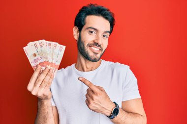 Genç İspanyol adam elinde 10 Kolombiya pezosu tutuyor. Gülümsüyor, mutlu bir şekilde parmakla işaret ediyor. 