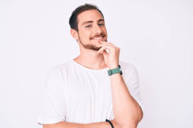 Gündelik beyaz tişört giyen genç yakışıklı kameraya kendinden emin kollarını kavuşturmuş ve çenesini kaldırmış bir şekilde bakıyor. Olumlu düşünmek. 