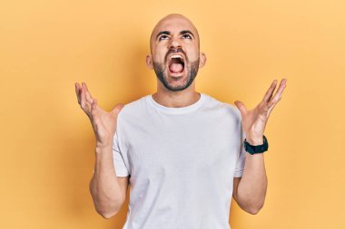 Sıradan beyaz tişört giyen genç kel adam deli gibi bağırıyor, agresif bir ifadeyle bağırıyor ve kollarını kaldırıyor. hüsran kavramı. 