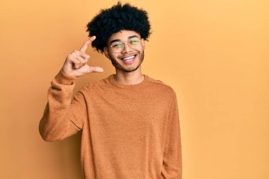 Afro saçlı, sıradan bir kazak giyen, gülümseyen, kendine güvenen, el hareketi yapan, parmaklarıyla işaret yapan ve kameraya bakan Afrikalı genç bir Amerikalı. ölçüm kavramı. 