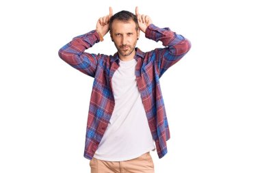 Genç ve yakışıklı bir adam günlük kıyafetler giyiyor. Komik hareketler yapıyor. Parmağını boynuz gibi kafasının üstünde gezdiriyor. 