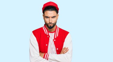 Sakallı, beyzbol forması giyen, kuşkucu ve gergin genç bir adam. Yüzünde çapraz kollu, onaylamayan bir ifade var. negatif kişi. 