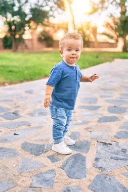 Sevimli ve mutlu küçük çocuk güneşli bir günde parkta eğleniyor. Güzel sarı saçlı erkek çocuk dışarıda oynuyor.