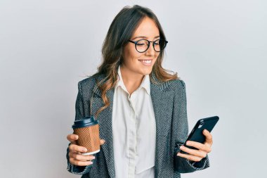 Genç esmer kadın akıllı telefon kullanıyor ve bir fincan kahve içiyor mutlu ve havalı bir gülümsemeyle gülümsüyor. diş gösterme. 