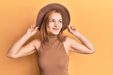 Şapkalı genç beyaz bir kadın gülümsüyor, yan tarafa bakıyor ve düşünüyor.. 